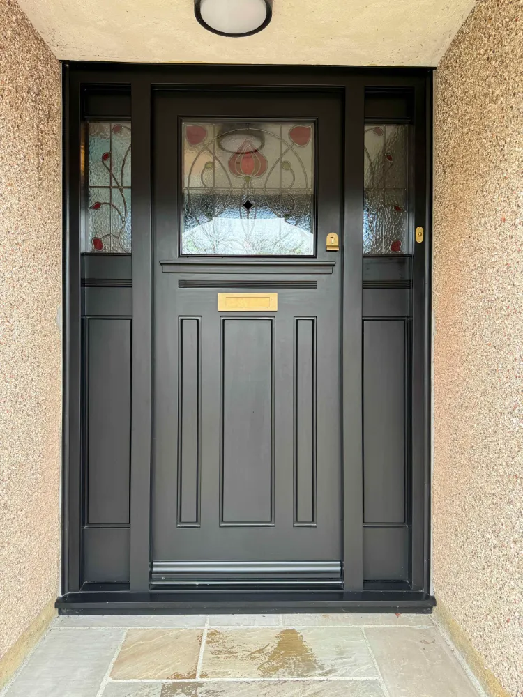 Black painted timber front door beneath a leaded glass fanlight