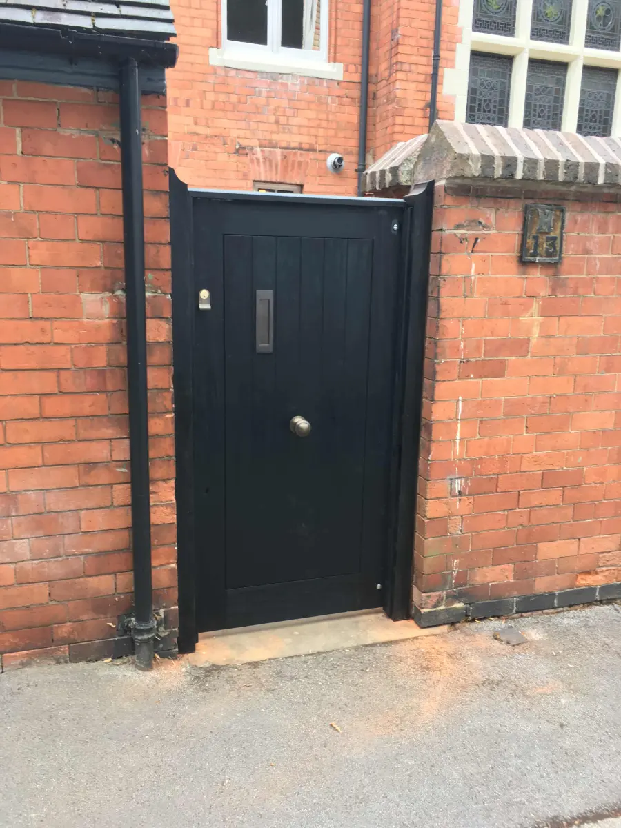 Simple black painted timber front door set into a red brick wall