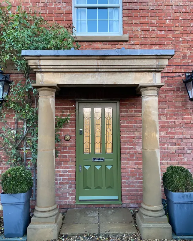 Green painted Edwardian timber front door with decorative glazed panels beneath a stone portico with columns