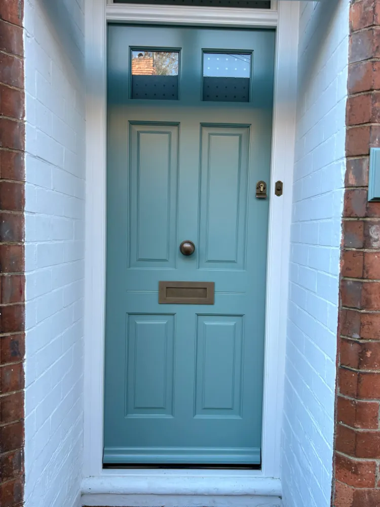 Teal painted six-panel Georgian-style timber front door with a brass knob and letter plate, set in a white brick reveal