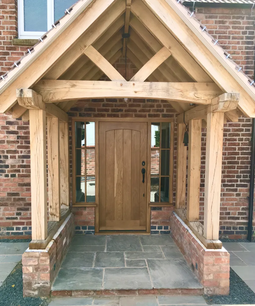Oak-framed open porch sheltering a natural oak front door on a brick house