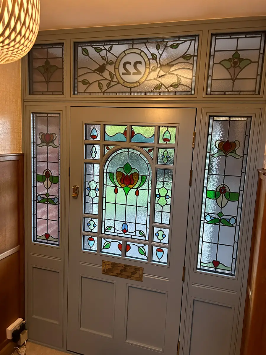 Panelled timber front door with a stained glass upper panel and matching leaded sidelights, seen from inside the hallway
