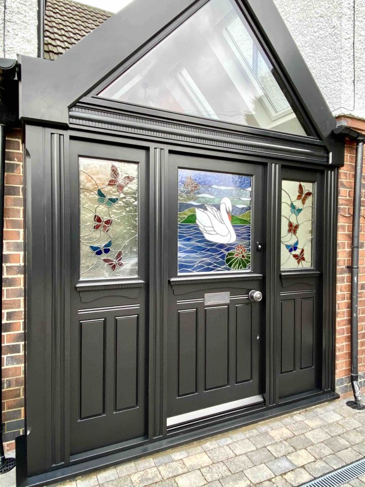 White front door with decorative stained glass panels featuring geometric patterns and a central vibrant owl design, framed by matching sidelights and a transom window.