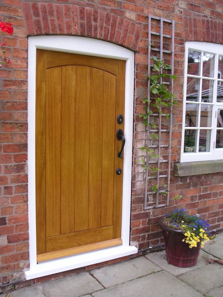 Black front door with an ornate arched stained glass panel featuring floral designs, flanked by matching side panels with decorative glass, set within a brick facade.