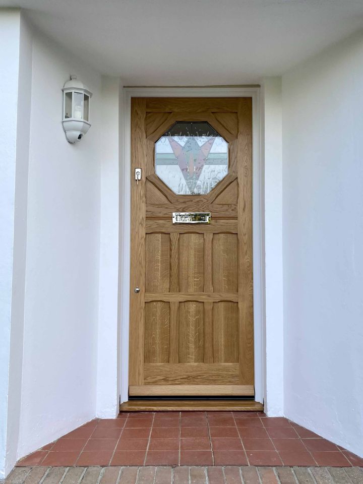 Blue front door with an intricate stained glass panel and matching side lights, set within a stone facade, flanked by topiary trees in terracotta pots.