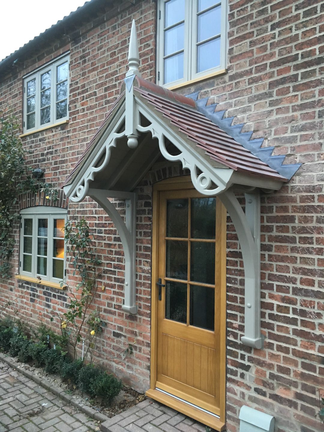 Side perspective of the Victorian porch, showcasing its arched supports, tile roof, and integration with brick façade and garden boxwood.