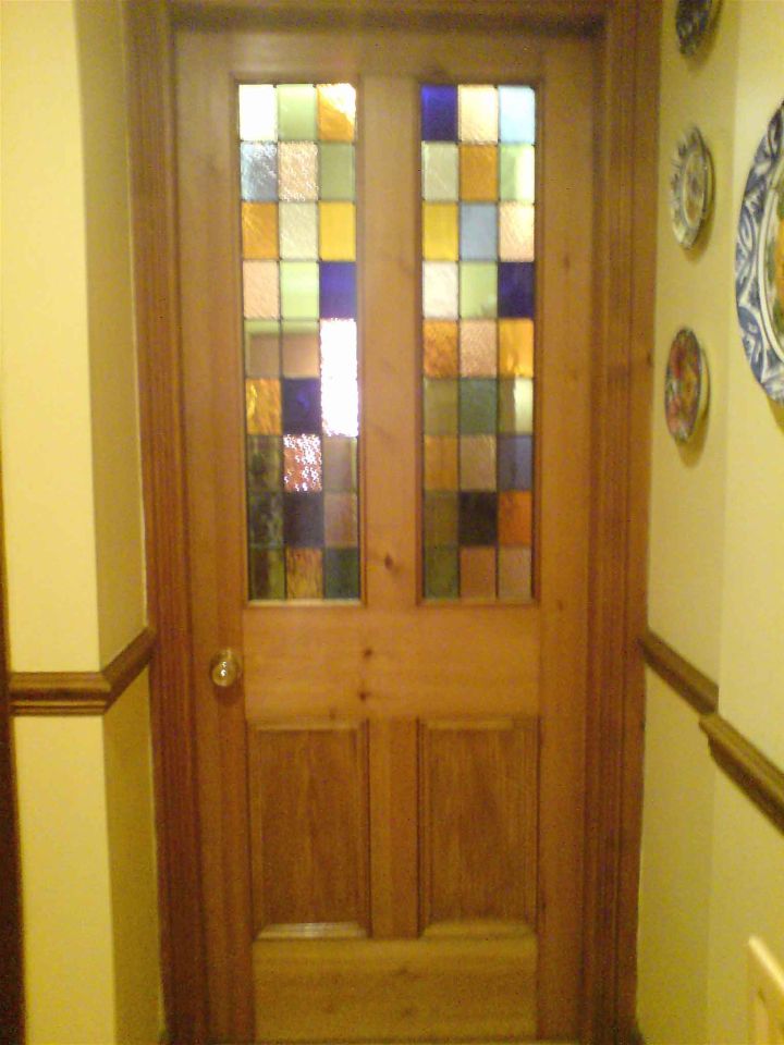 Elegant grey front door with ornate stained glass panels and matching sidelights and transom, featuring colourful geometric and floral designs, framed by an arched porch.