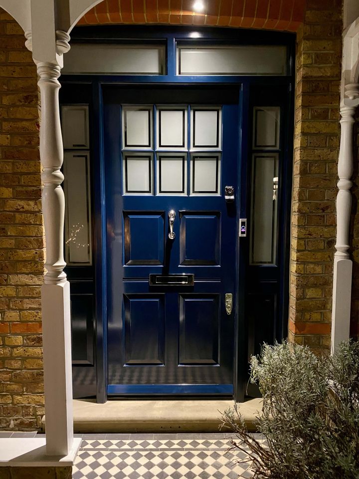 Black front door with an ornate arched stained glass panel featuring floral designs, flanked by matching side panels with decorative glass, set within a brick facade.