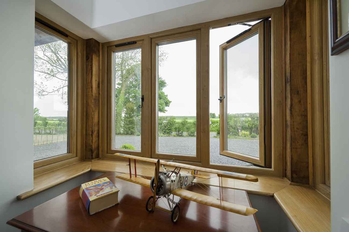White bay window with multiple glass panes, framed by classical columns and set on a brick base, overlooking a garden.