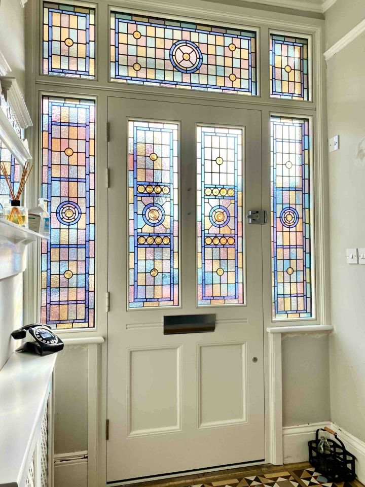 Sage green double door with intricate stained glass panels featuring floral motifs in red, blue, and green, framed by matching sidelights.