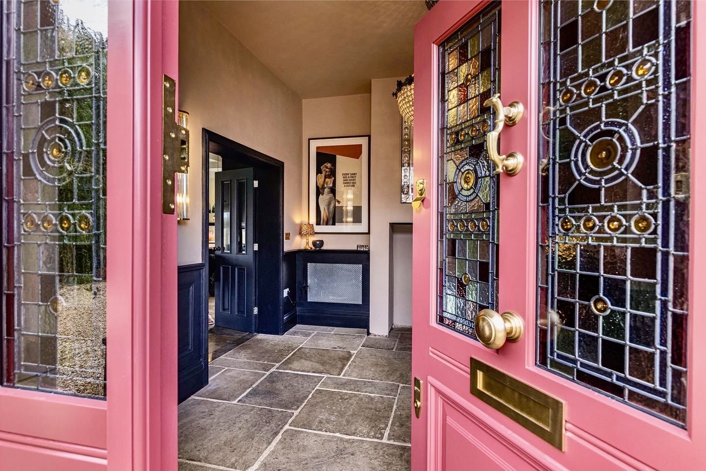 Wooden double doors with decorative stained glass panels featuring floral designs in green, red, and yellow, framed by arched tops and secure brass locks.