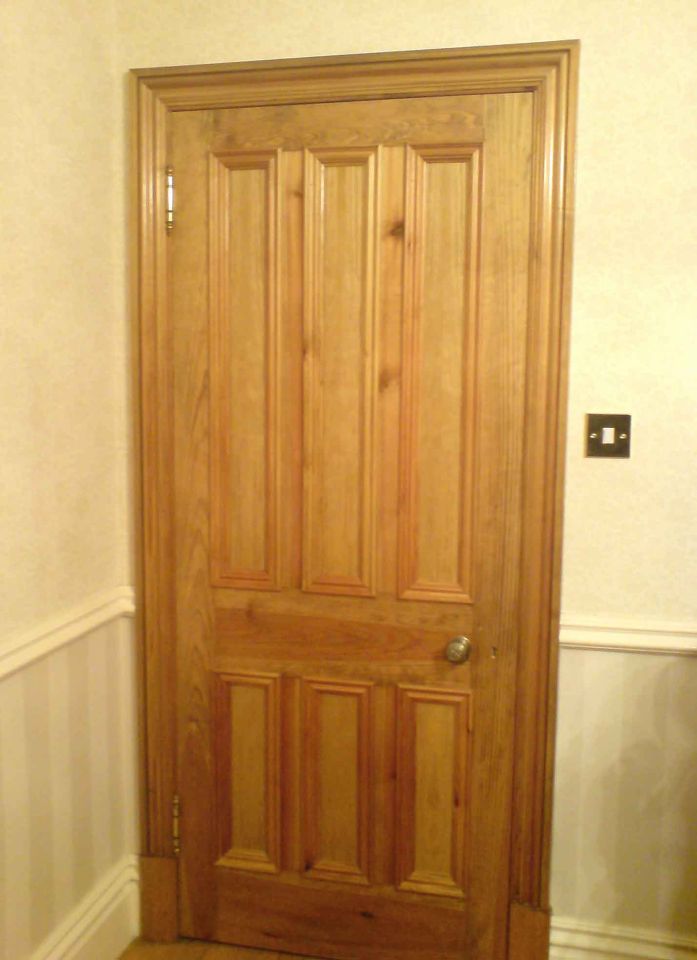 Blue front door with an intricate stained glass panel and matching side lights, set within a stone facade, flanked by topiary trees in terracotta pots.