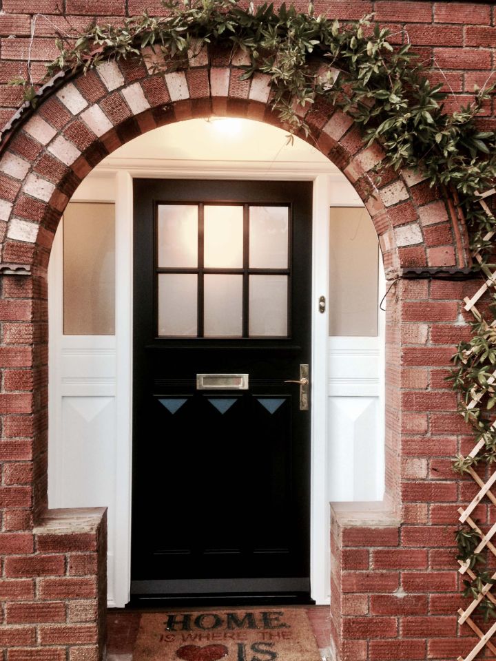 Blue front door with an intricate stained glass panel and matching side lights, set within a stone facade, flanked by topiary trees in terracotta pots.