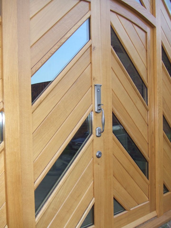 Blue front door with an intricate stained glass panel and matching side lights, set within a stone facade, flanked by topiary trees in terracotta pots.